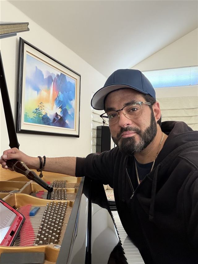 Rob Vela at a grand piano, tuning hammer in hand